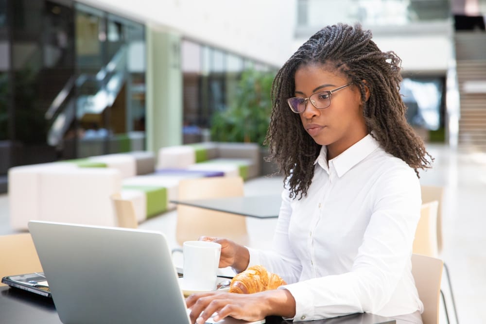Black American woman at a table analyzing customers' data on a laptop.